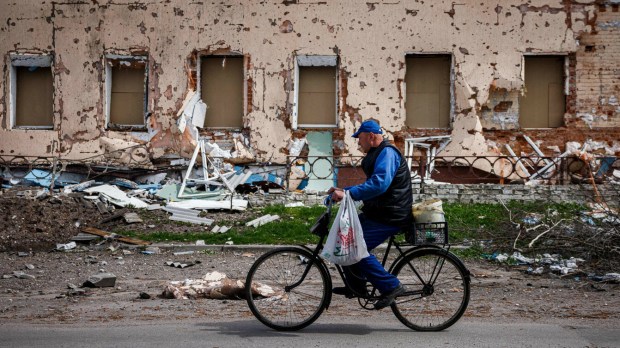 rowerzysta przejeżdża obok budynku zniszczonego przez Rosjan w jednej z wiosek na Ukrainie