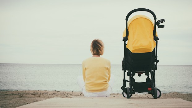 samotna matka siedzi na plaży obok wózka dziecięcego