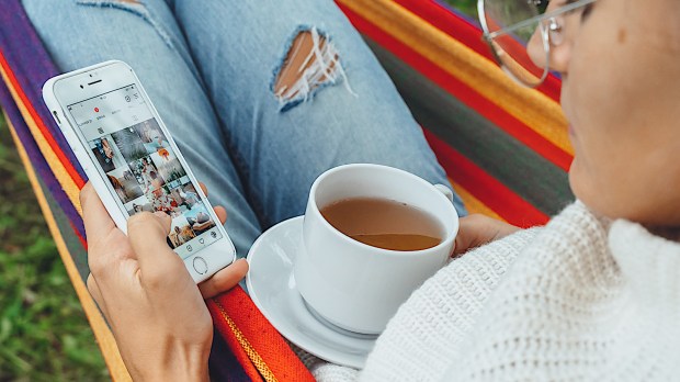 młoda dziewczyna przegląda Instagrama leżąc w hamaku i pijąc herbatę