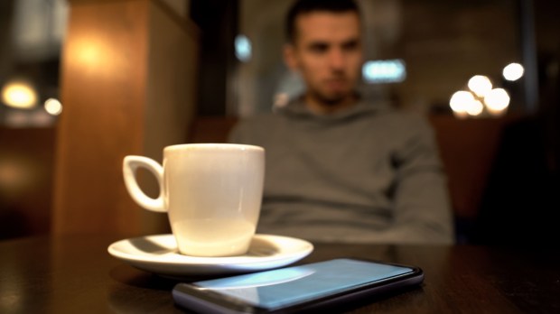 samotny mężczyzna siedzi w kawiarni, a przed na stole stoi filiżanka kawy espresso i leży smartfon