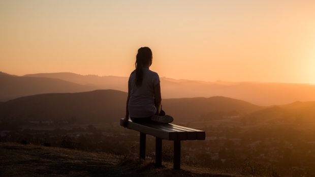 a young girl sits on a bench and looks into the distance during twilight
