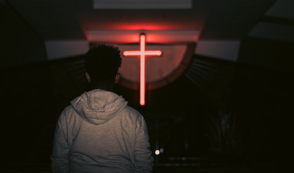 young man looks at red neon cross