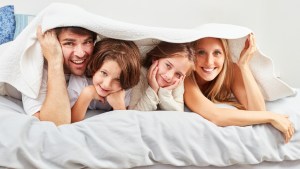 Uśmiechnięci rodzice chowają się pod kocem razem z dwójką radosnych dzieci