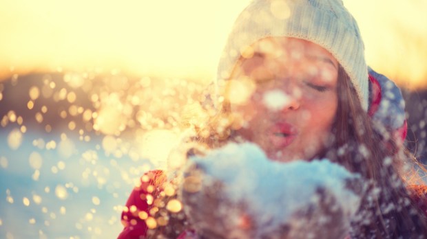 Radosna dziewczyna dmucha w śnieg, który leży na jej rękach